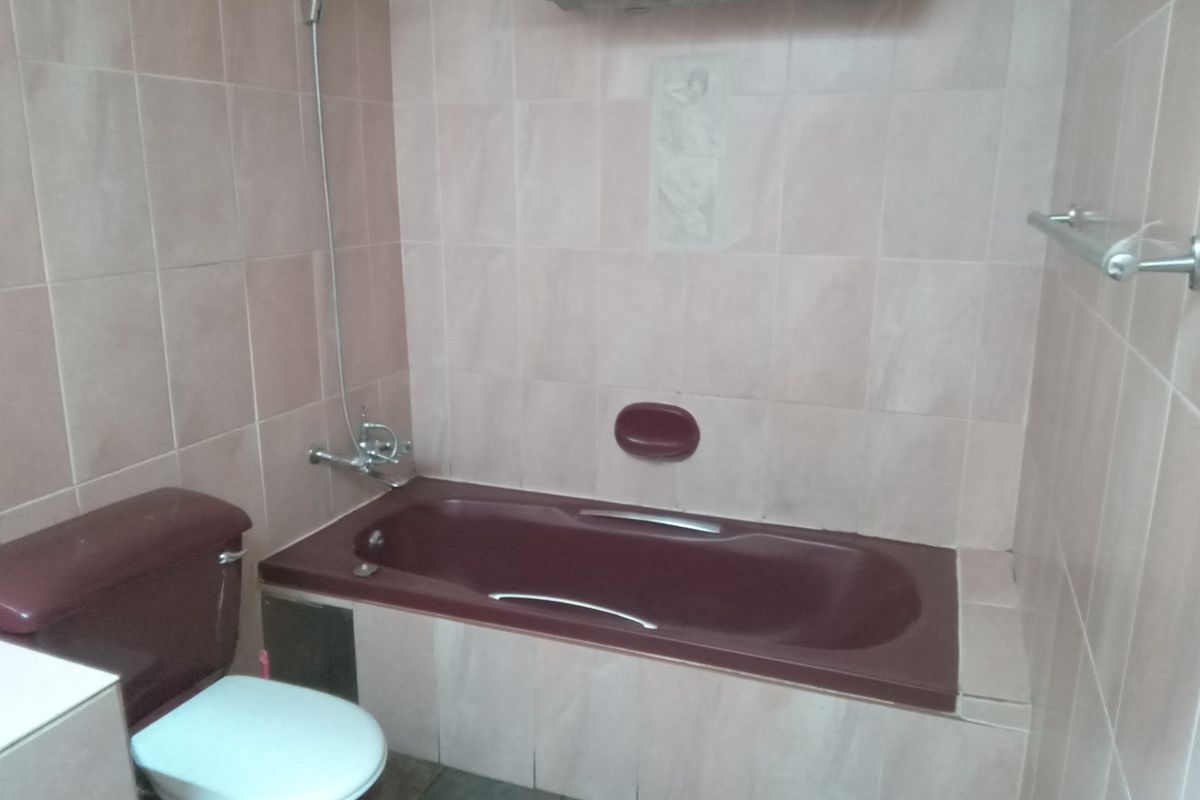 A dated bathroom featuring a built-in bathtub, toilet, and wall tiling, offering potential for a modern renovation.