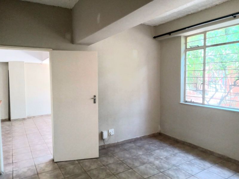 An empty bedroom featuring tiled flooring, security bars on the window, and neutral wall finishes, offering a blank canvas for personalization.