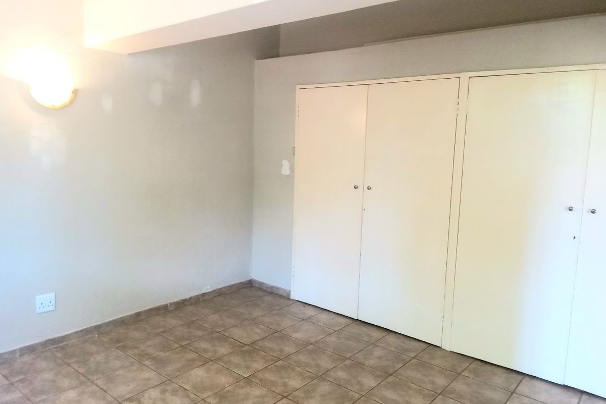 An empty bedroom featuring tiled flooring and built-in cupboards, requiring minor cosmetic attention to the wall finishes.