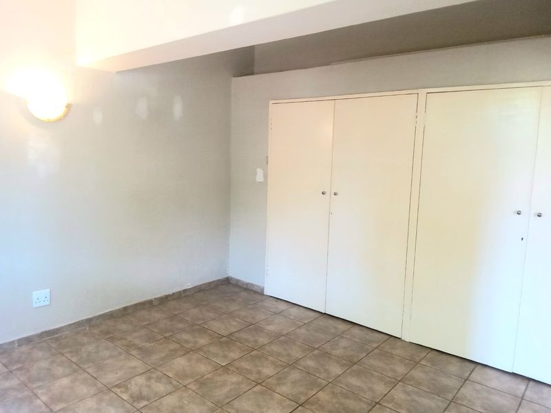 An empty bedroom featuring tiled flooring and built-in cupboards, requiring minor cosmetic attention to the wall finishes.