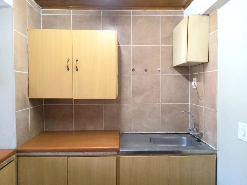 A compact kitchen area featuring laminate countertops, a stainless steel sink, and wall-mounted cabinetry with tiled splashbacks.