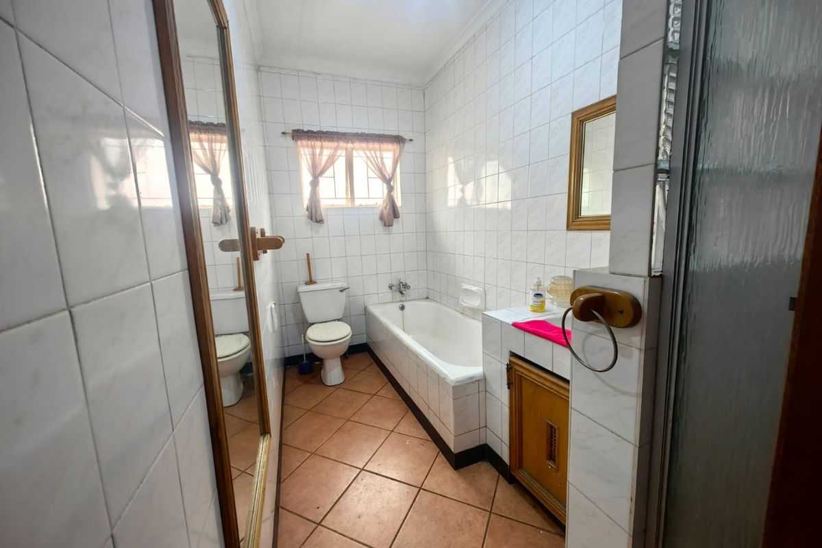 A dated bathroom featuring a built-in bathtub, toilet, and vanity cabinet with full-height wall tiling and terracotta-style floor tiles.