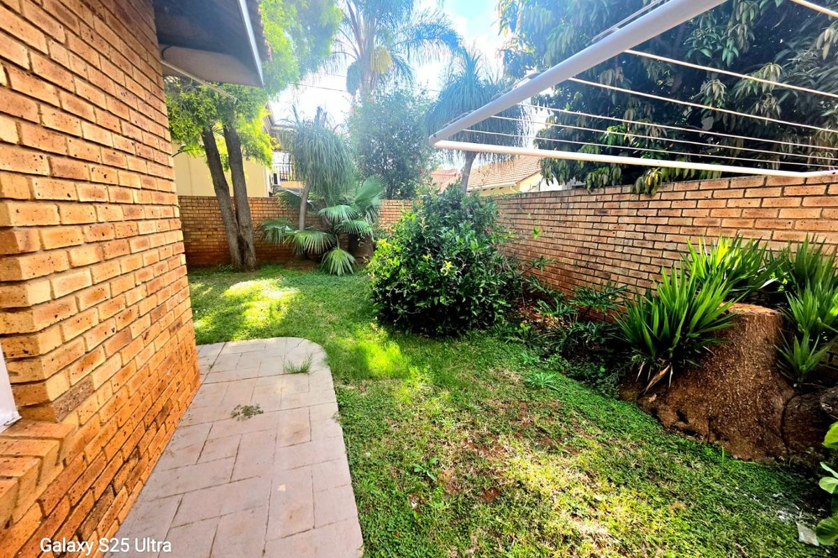 A private rear garden area featuring a paved walkway, brick boundary walls, and a fixed washing line, surrounded by established trees and shrubs.
