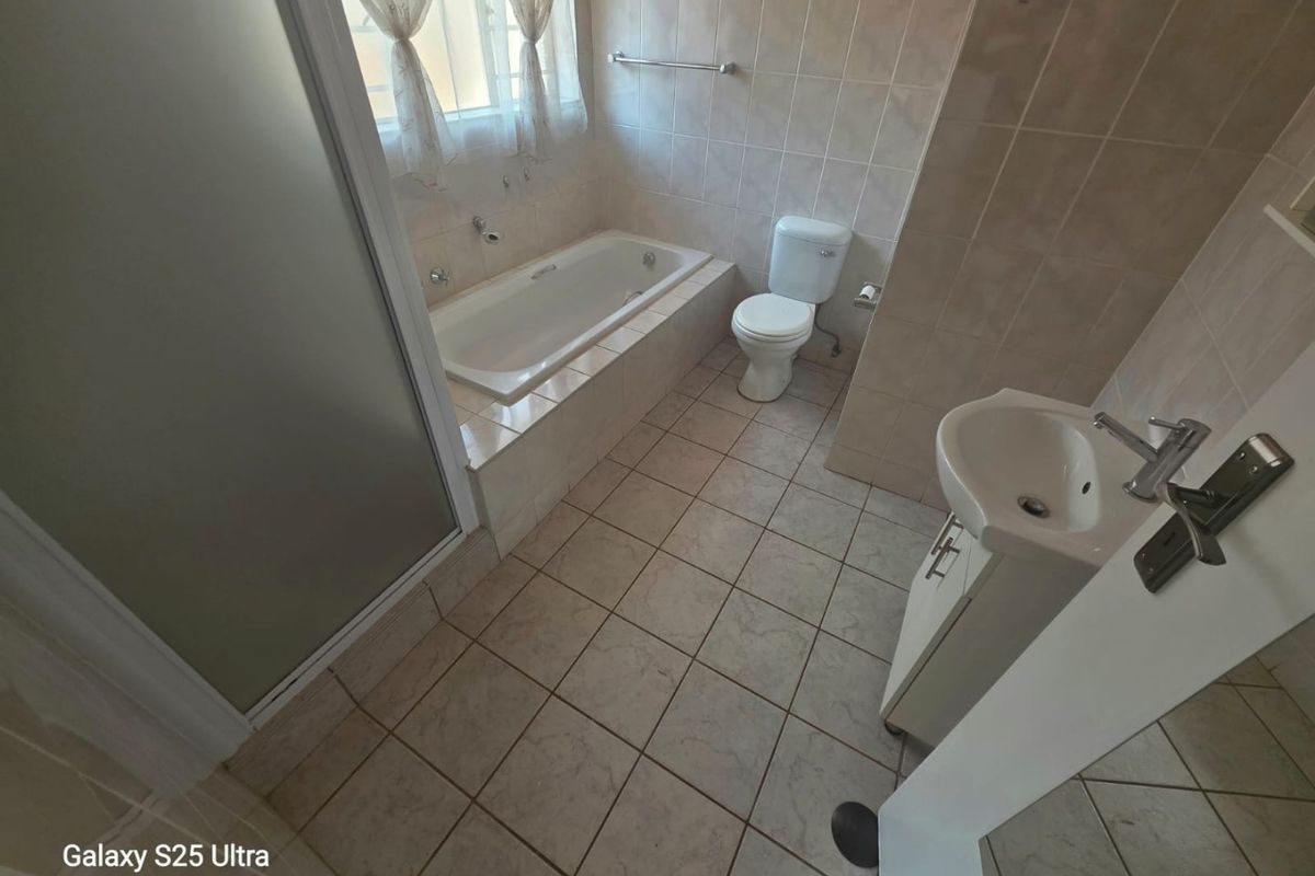A functional bathroom featuring a built-in bathtub, separate shower enclosure, toilet, and a vanity unit with a washbasin, finished with neutral wall and floor tiles.