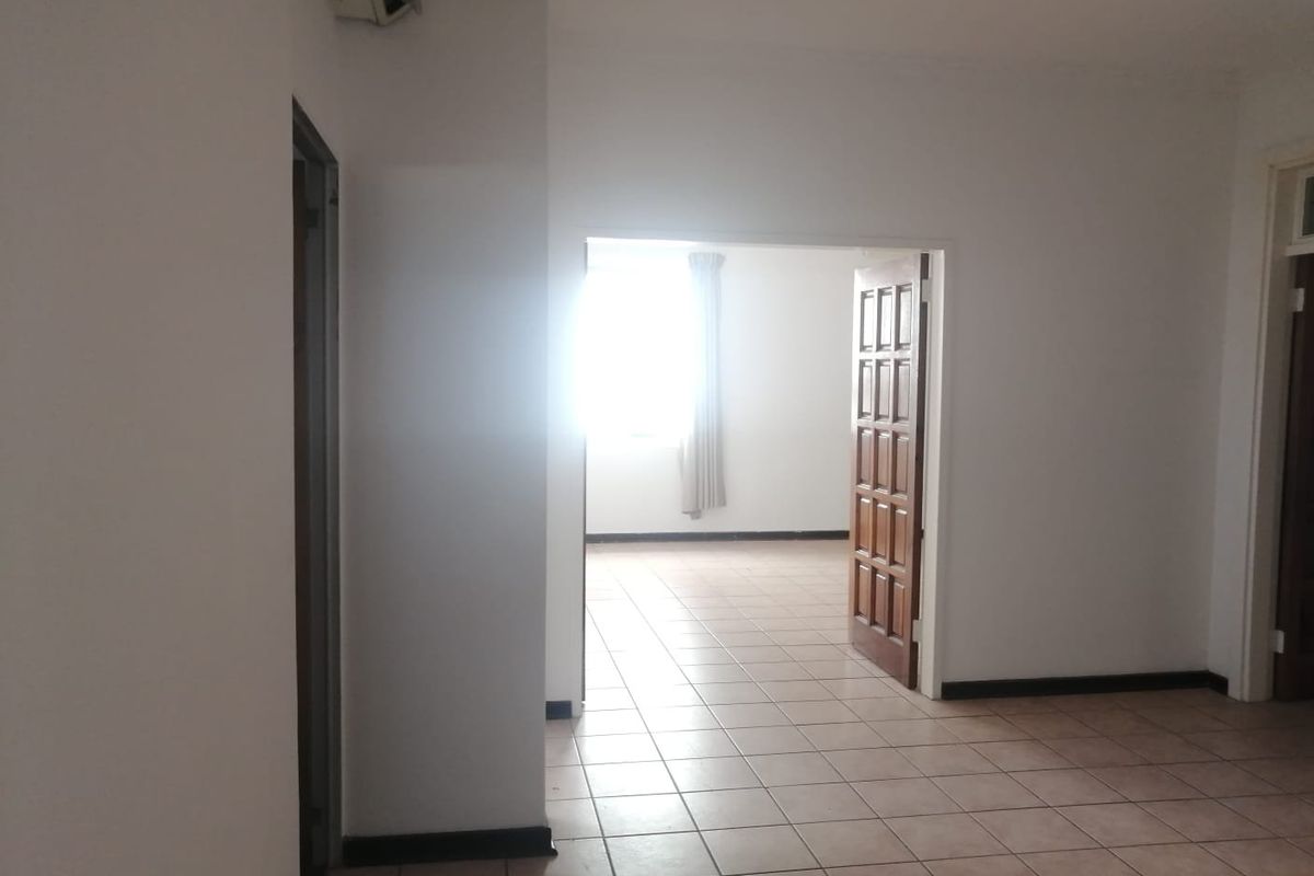 An interior view of a commercial space featuring tiled flooring, neutral walls, and a wooden door leading to an adjacent room.