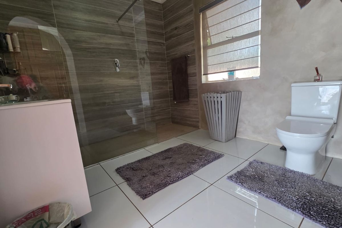 A modern bathroom featuring a walk-in shower with tiled walls, a white toilet, and large format floor tiles.