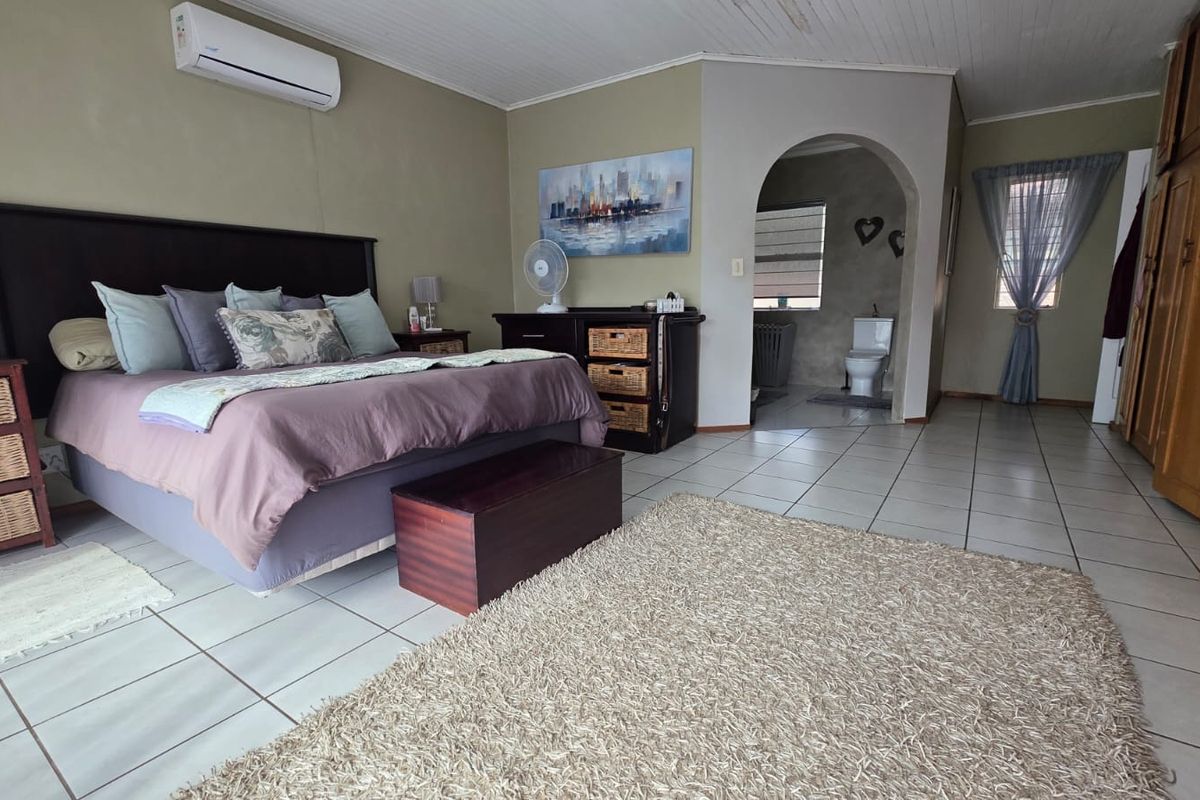 Spacious bedroom featuring tiled flooring, built-in cupboards, and an open archway leading to an en-suite bathroom, equipped with a wall-mounted air conditioning unit.
