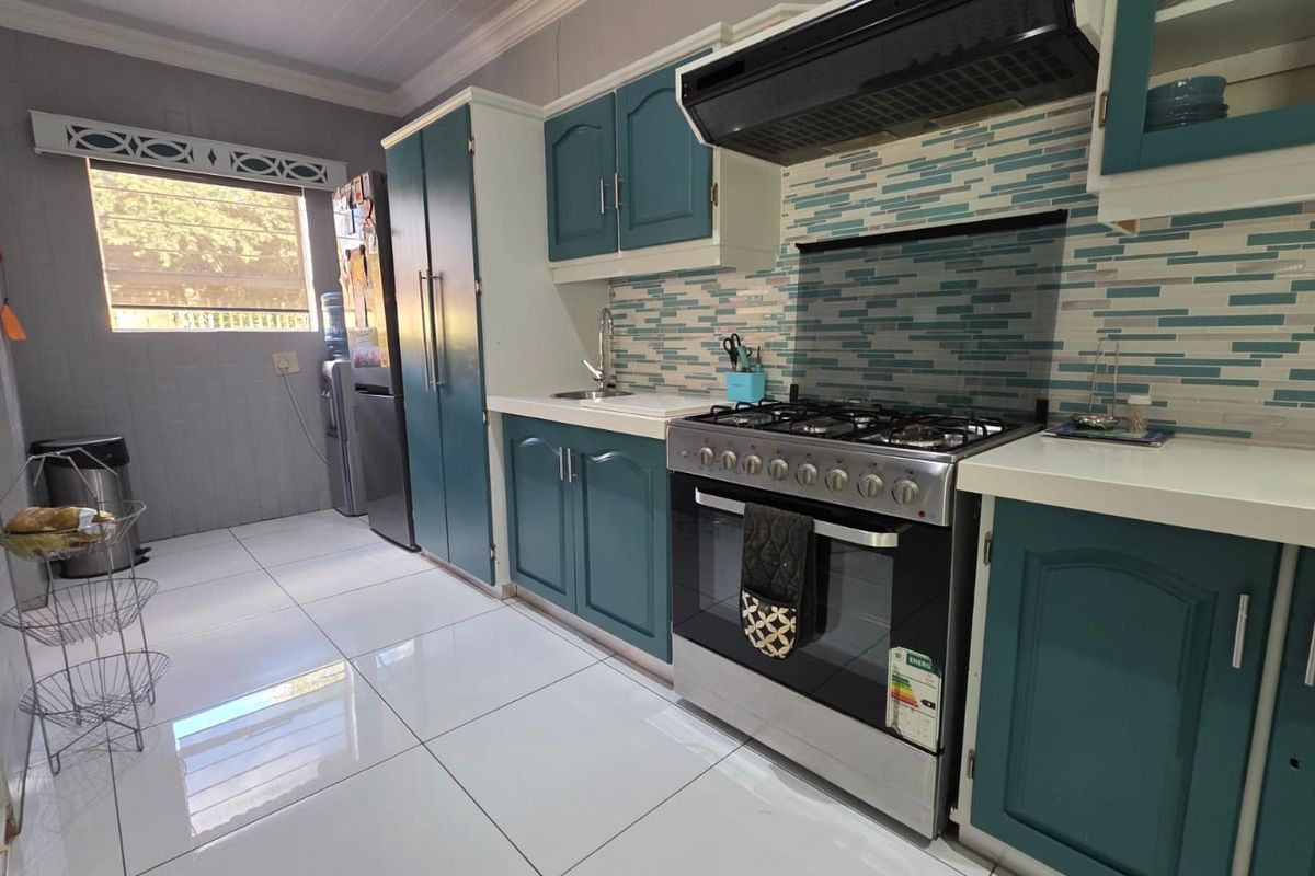 A functional kitchen featuring teal cabinetry, a gas stove with an extractor fan, a tiled backsplash, and polished floor tiles.