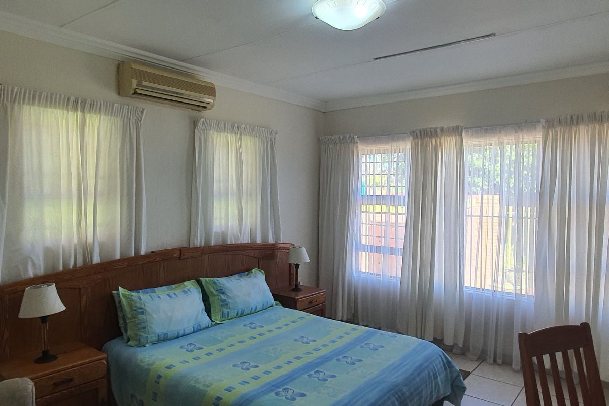 A well-lit bedroom featuring tiled flooring, a wall-mounted air conditioning unit, and security bars on the windows.