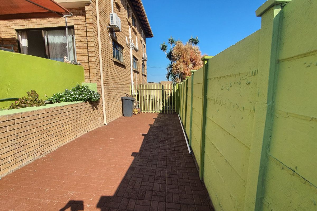 A side exterior area featuring brick paving, a painted precast concrete boundary wall, and a metal security gate.