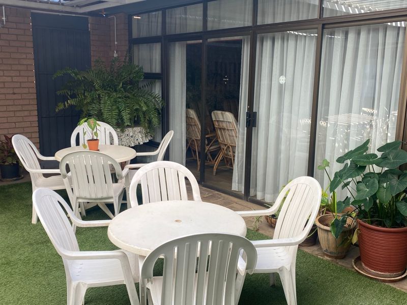 A covered patio area featuring artificial turf flooring, brick wall accents, and large sliding glass doors providing access to the interior living space.