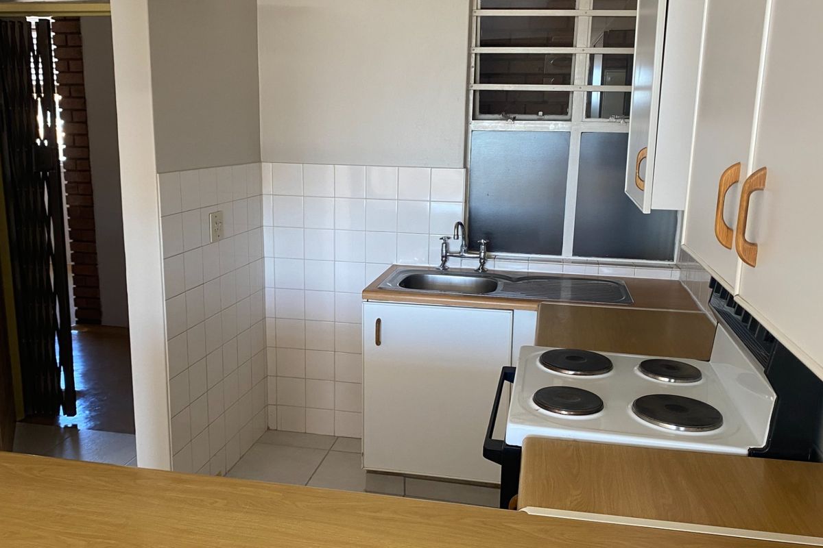 A compact kitchen featuring white cabinetry, laminate countertops, a stainless steel sink, and a freestanding electric stove with tiled splashback.