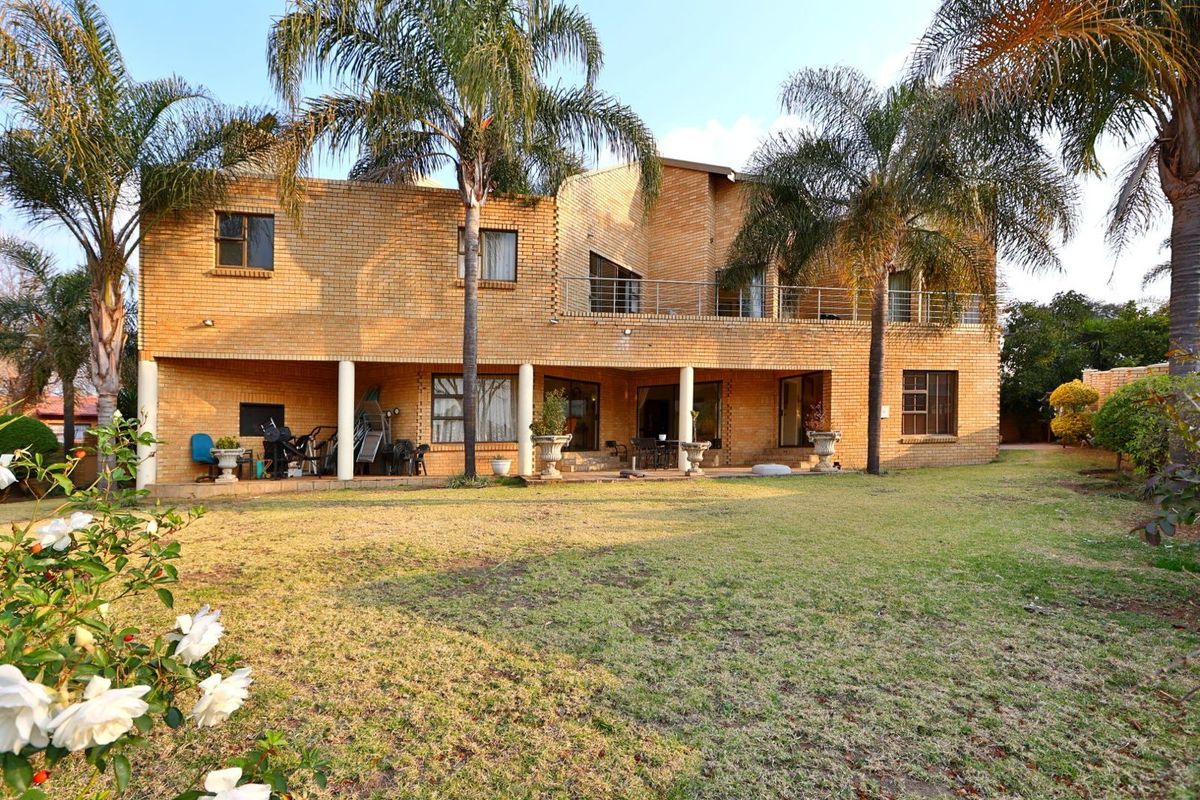 Rear view of a double-story face brick house featuring a covered ground-floor patio, an upper-level balcony with metal railings, and a spacious garden.