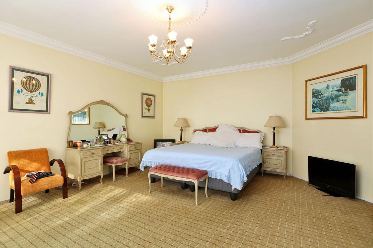 Spacious bedroom featuring classic ceiling cornicing, a decorative ceiling rose with chandelier, and wall-to-wall carpeting.