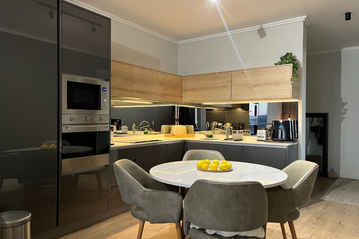 Modern kitchen featuring high-gloss cabinetry, built-in oven and microwave, and a stylish mirrored splashback with integrated lighting.