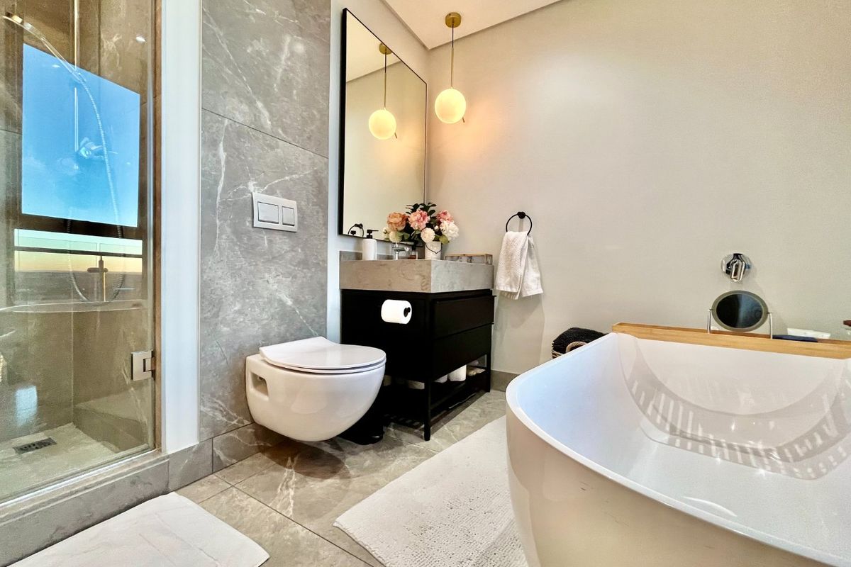 Modern luxury bathroom featuring a freestanding bathtub, glass-enclosed shower, wall-mounted toilet, and a sleek vanity with marble-look tiling throughout.