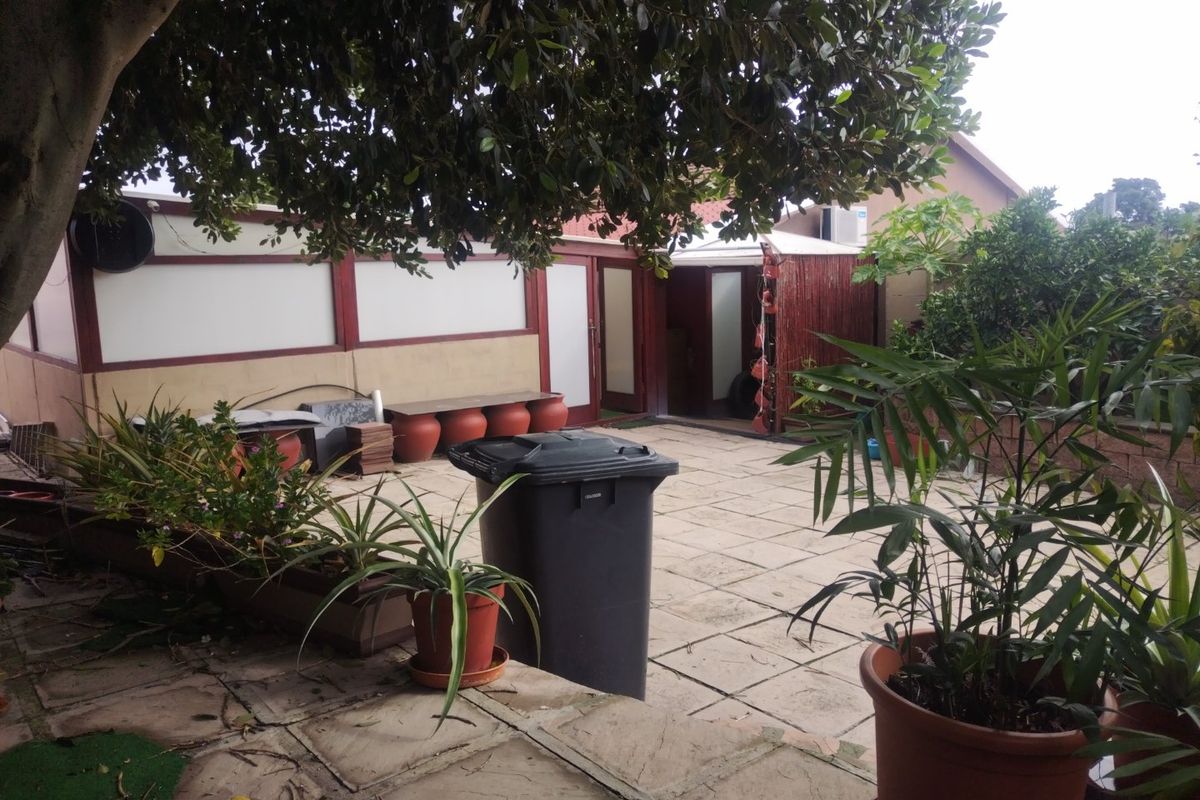 Rear exterior area featuring a paved patio space, boundary wall, and mature tree, offering potential for outdoor living improvement.