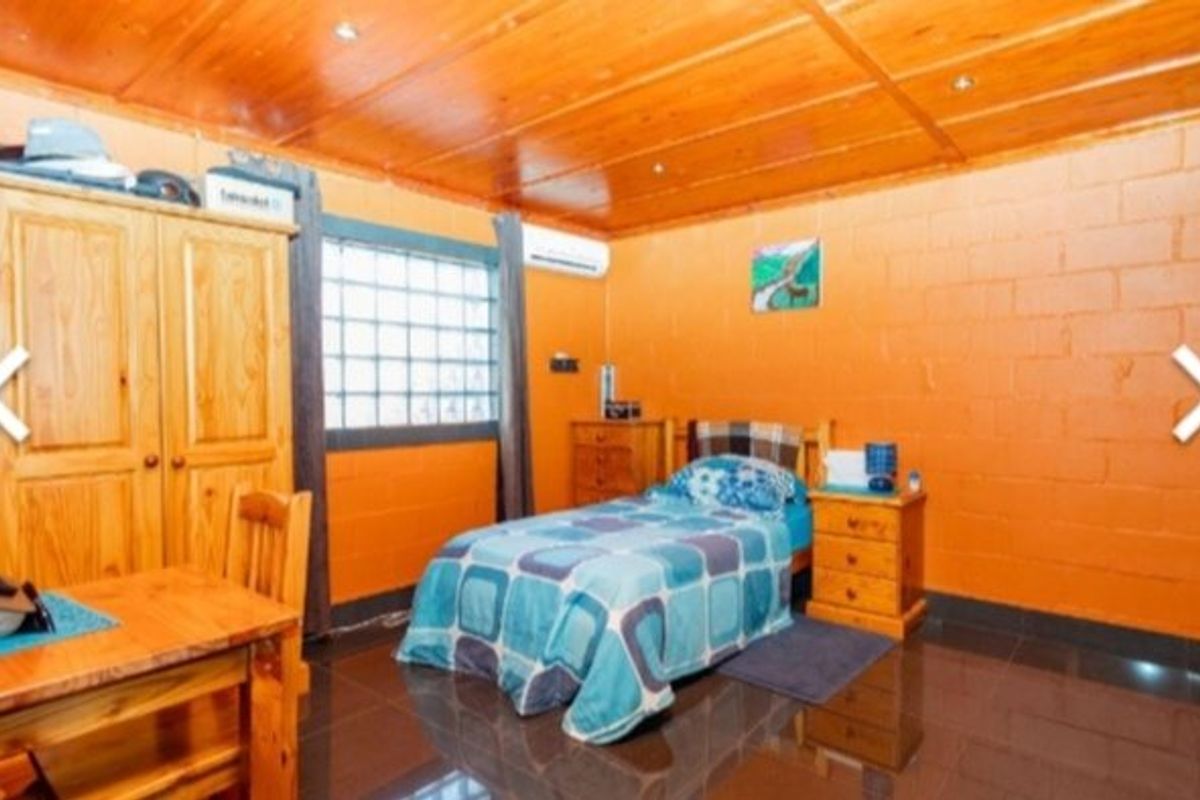 A bedroom featuring a timber ceiling, tiled flooring, and a glass block window, equipped with a wall-mounted air conditioning unit.