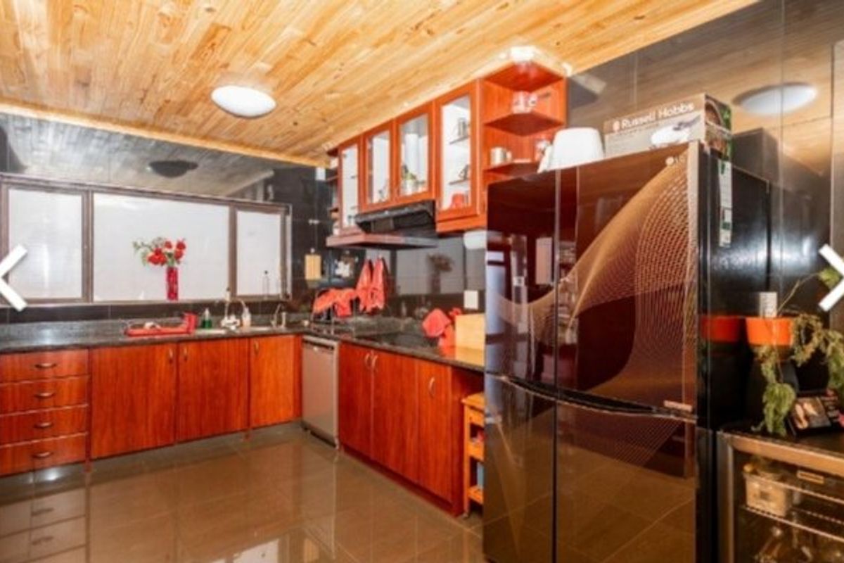 A functional kitchen featuring warm wooden cabinetry, granite countertops, a double sink, and a distinctive wooden ceiling with tiled flooring.