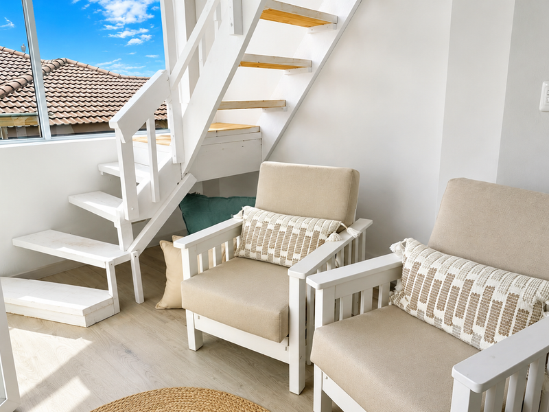 A bright living area featuring a modern timber staircase, light laminate flooring, and large sliding glass doors providing natural light and outdoor access.