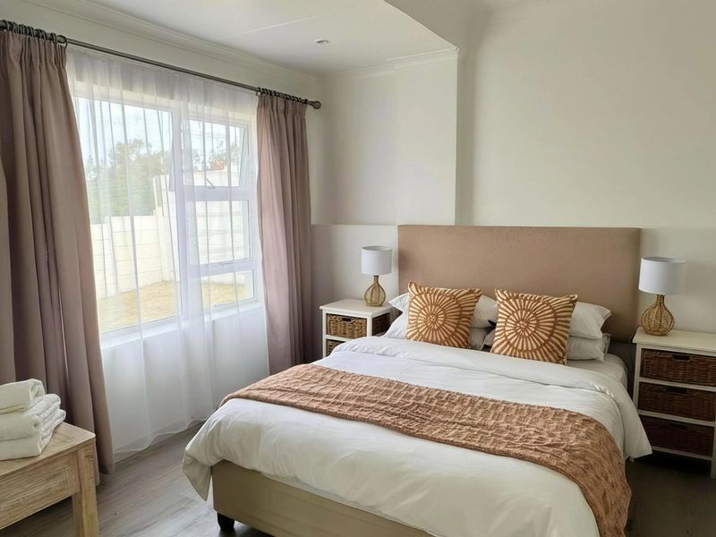 A well-maintained bedroom featuring neutral tones, laminate flooring, and a large window providing natural light.