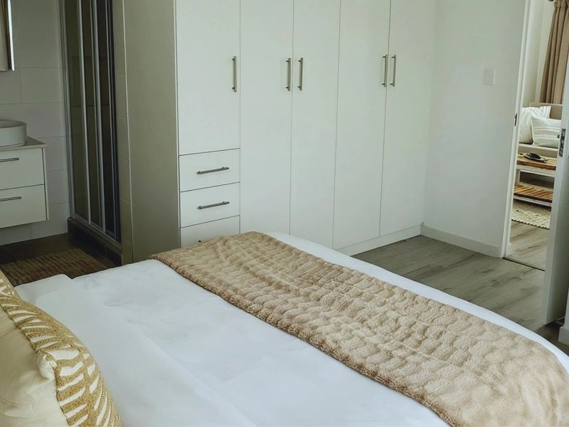 A well-maintained bedroom featuring built-in cupboards, laminate flooring, and an integrated en-suite bathroom with a modern vanity basin.