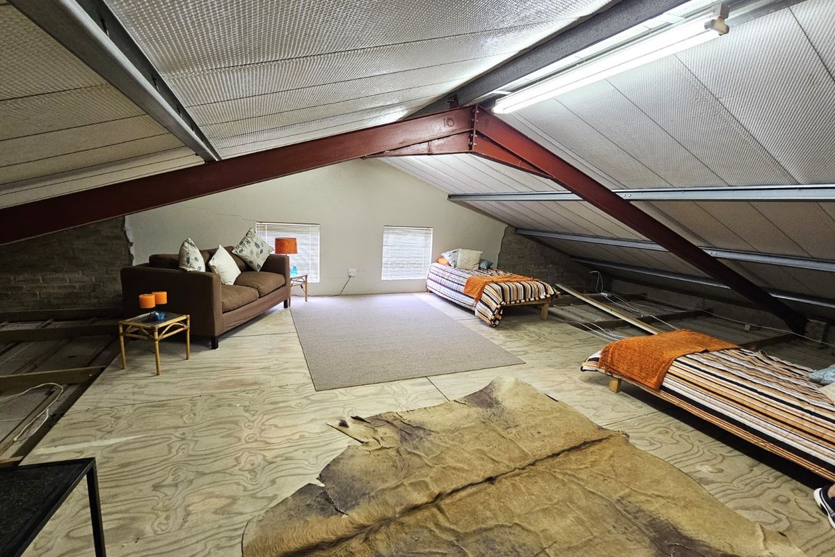 Spacious attic-style bedroom featuring exposed steel roof trusses, insulated panels, and plywood flooring, offering a rustic, industrial-style living space.