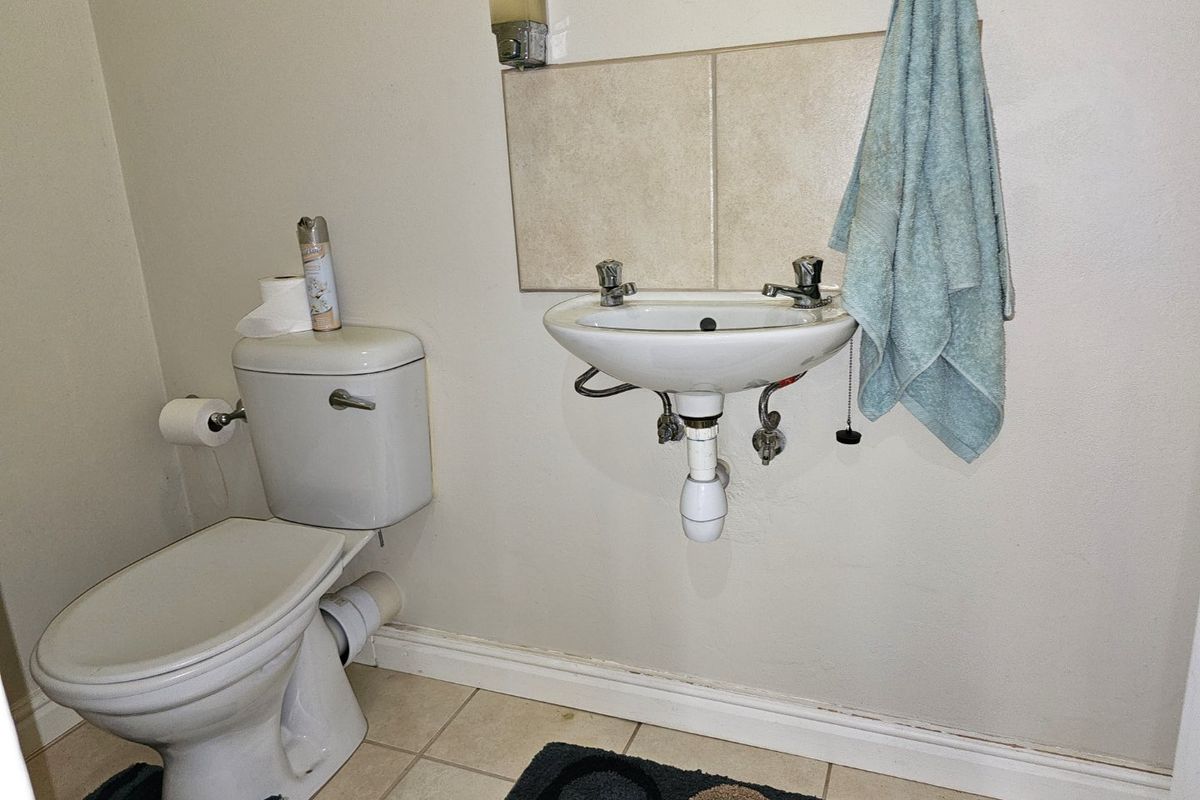 A functional guest bathroom featuring a wall-mounted basin, standard toilet, and neutral ceramic tiling.