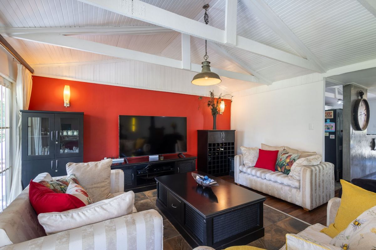 A cozy living room featuring a vaulted ceiling with exposed white timber beams, tiled flooring, and a bold red accent wall.