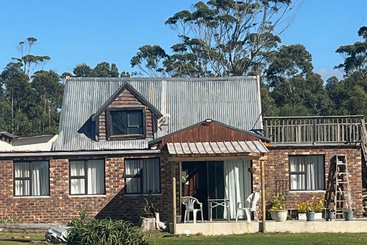 Rear view of a rustic facebrick farm cottage featuring a corrugated iron roof, a covered patio area, and an upper-level balcony.