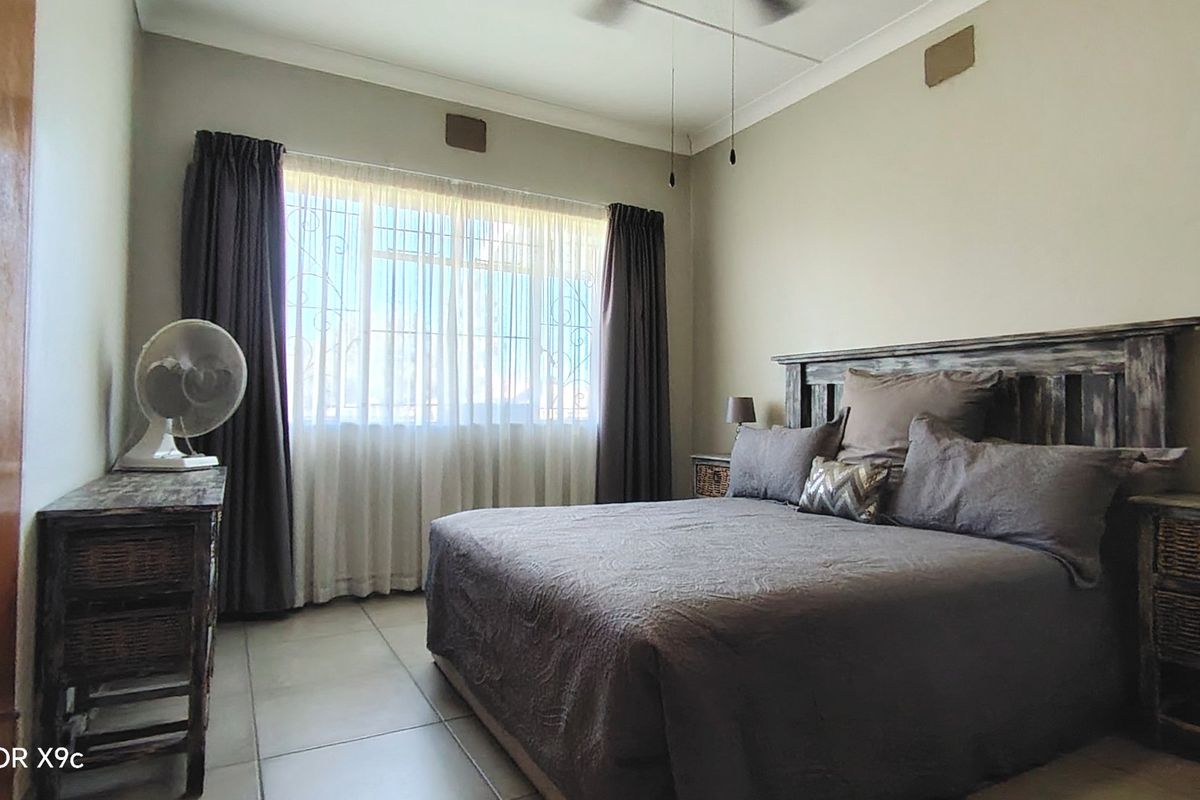 A well-lit bedroom featuring tiled flooring, neutral wall finishes, and a large window with curtain treatments.