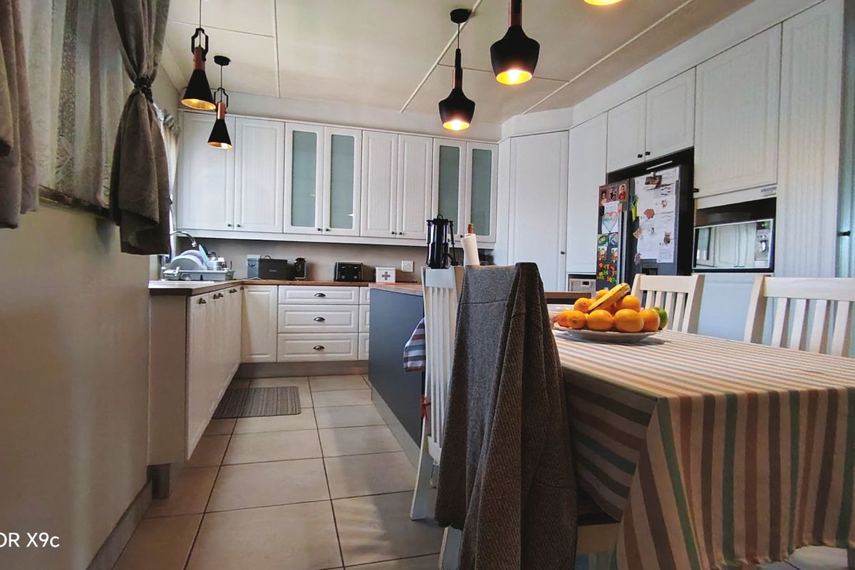 A well-lit kitchen featuring white cabinetry, tiled flooring, and a central dining area with modern pendant lighting.