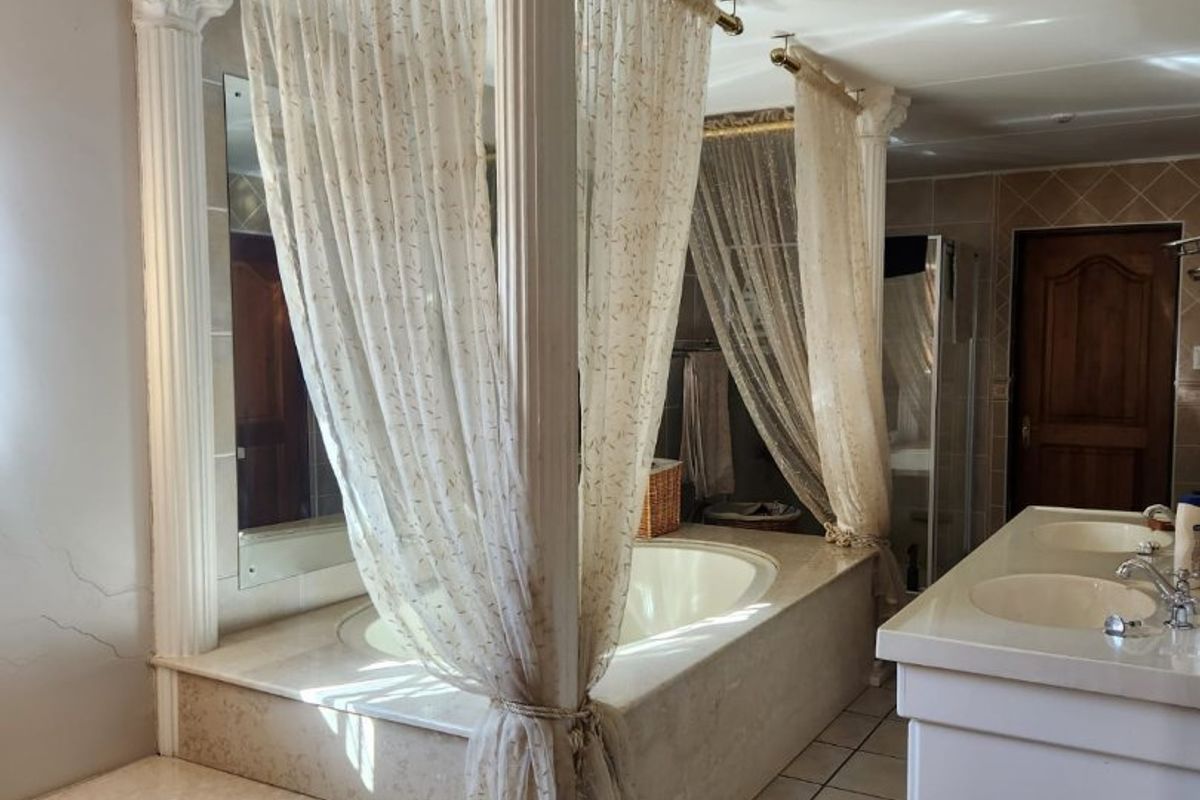Spacious bathroom featuring a raised built-in bathtub with decorative columns, double vanity, and tiled flooring.