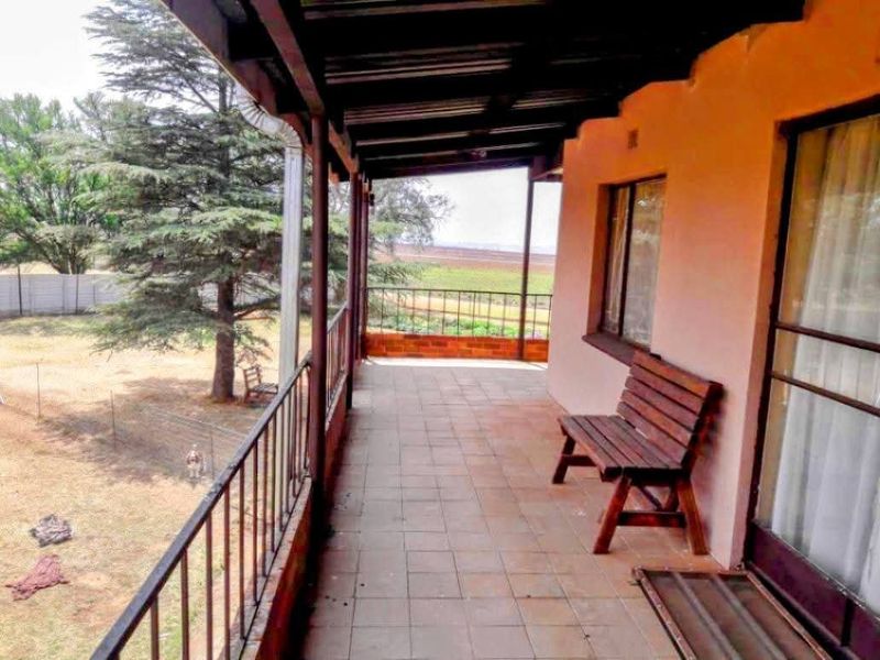 A covered outdoor patio featuring tiled flooring and metal railings, overlooking the farm grounds.