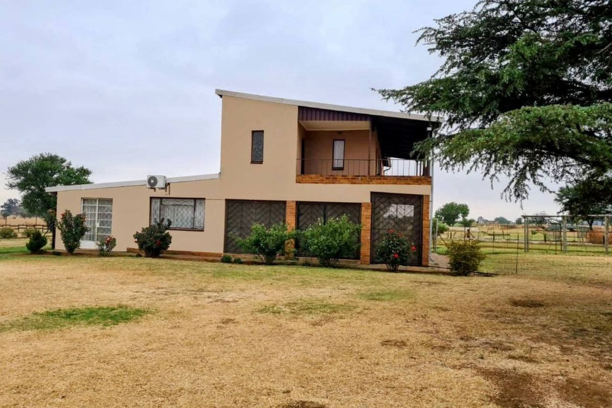 Rear view of a two-story farm house featuring a balcony, security gates, and sliding doors set within a large open landscape.
