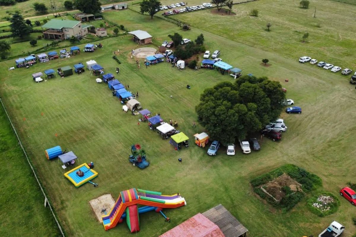 Aerial view of a large farm property featuring expansive open grass fields, mature trees, and perimeter fencing, currently utilized for outdoor event hosting.