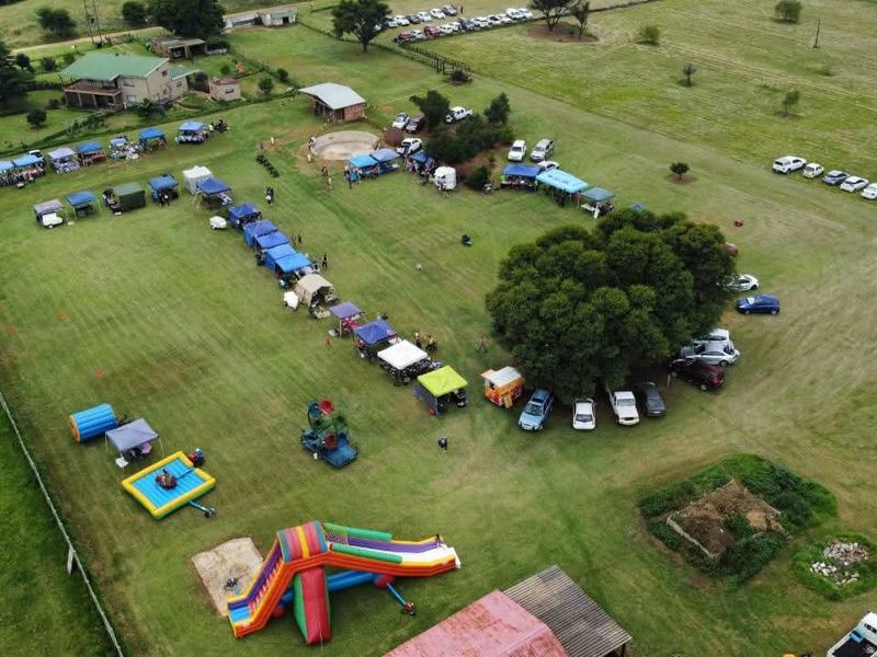 Aerial view of a large farm property featuring expansive open grass fields, mature trees, and perimeter fencing, currently utilized for outdoor event hosting.