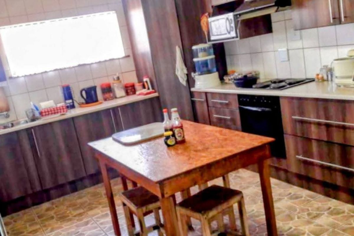 A functional kitchen featuring dark wood-finish cabinetry, tiled backsplash, built-in oven, gas hob, and extractor fan with tiled flooring throughout.