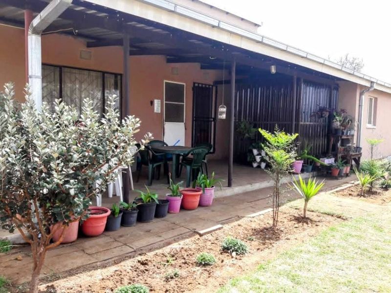 A covered outdoor patio area featuring concrete flooring and metal structural supports, providing a functional space for outdoor relaxation overlooking the garden.