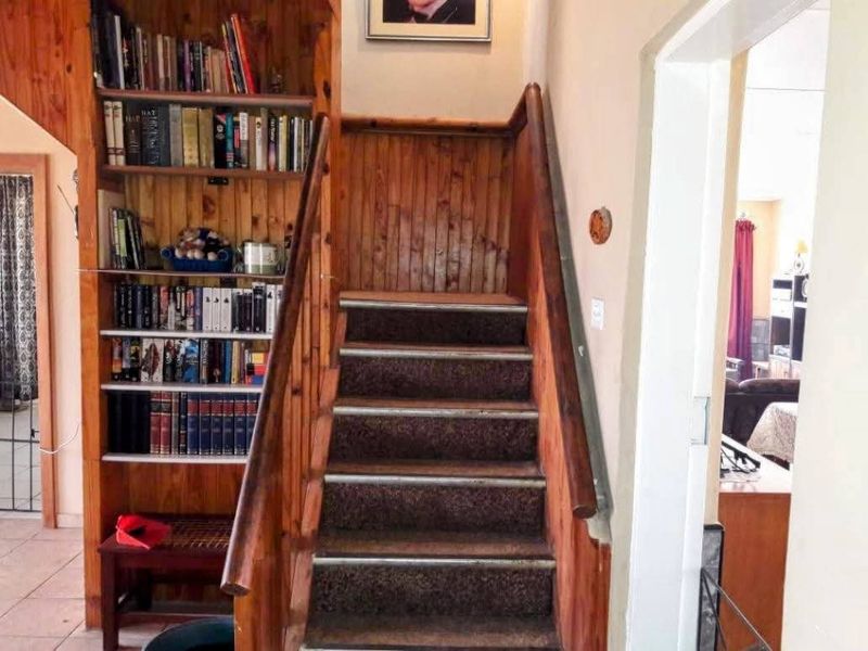 A hallway featuring a wooden staircase with built-in shelving and wood paneling, showing signs of wear and dated finishes.