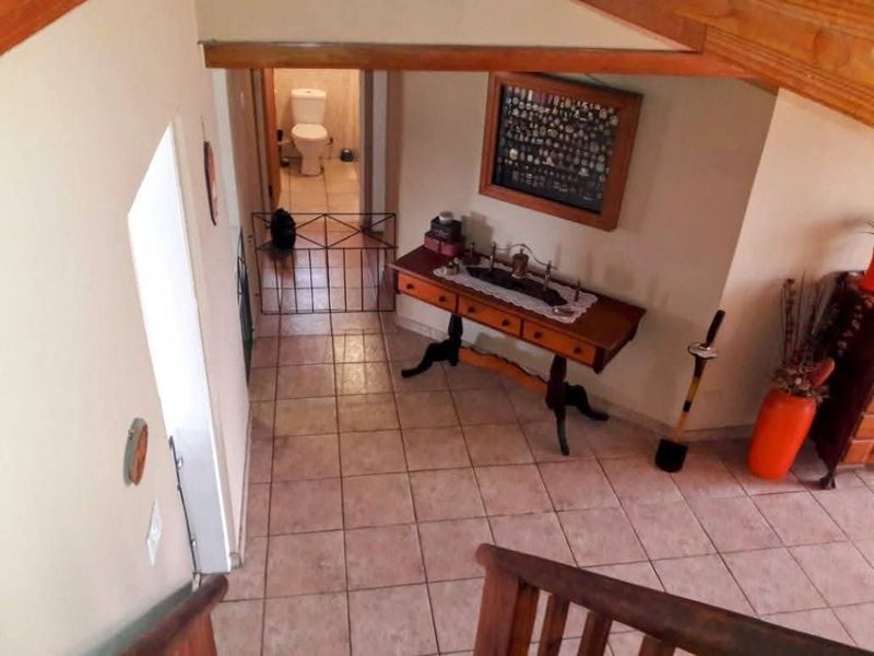 A tiled hallway area viewed from the staircase, featuring wooden architectural details and access to a bathroom.