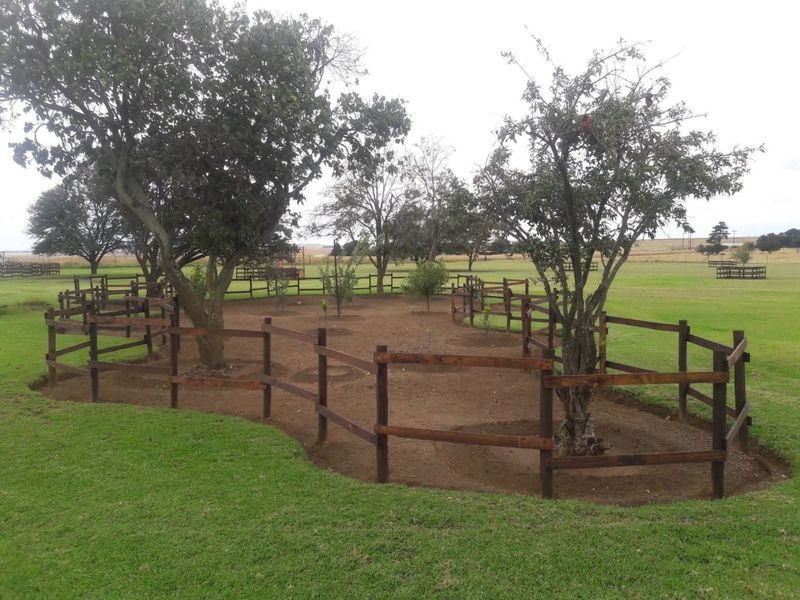 A well-maintained farm garden featuring timber post and rail fencing enclosing mature trees and landscaped garden beds set within a large grassy area.