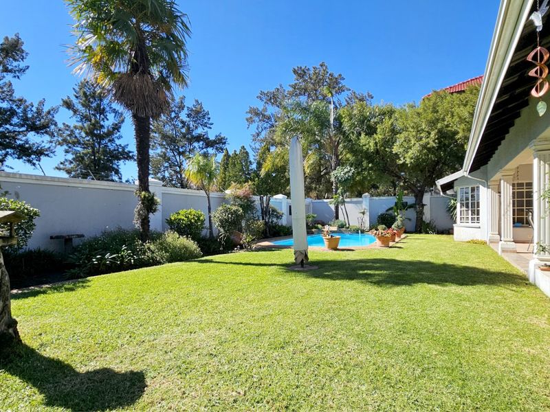 Spacious rear garden featuring a well-maintained lawn, a swimming pool, and a covered patio area, enclosed by a secure perimeter wall.