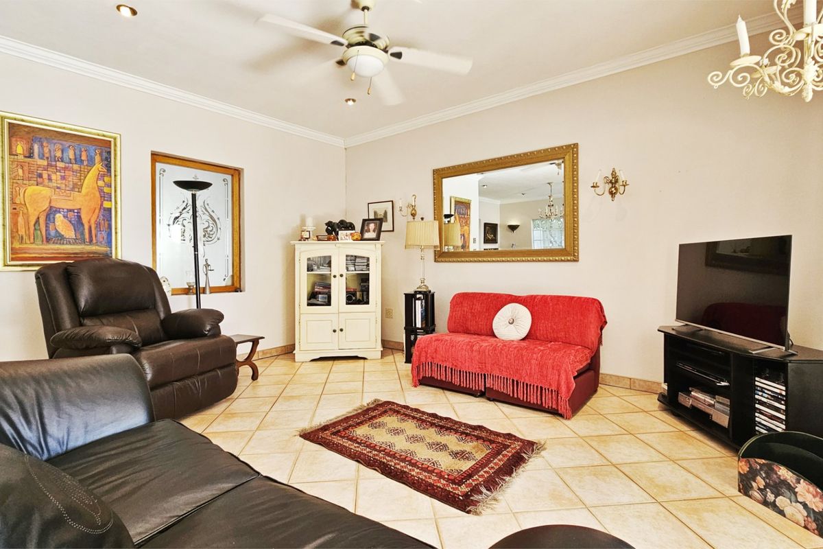 A spacious living room featuring tiled flooring, a ceiling fan, and decorative cornice detailing, offering a comfortable and functional layout.