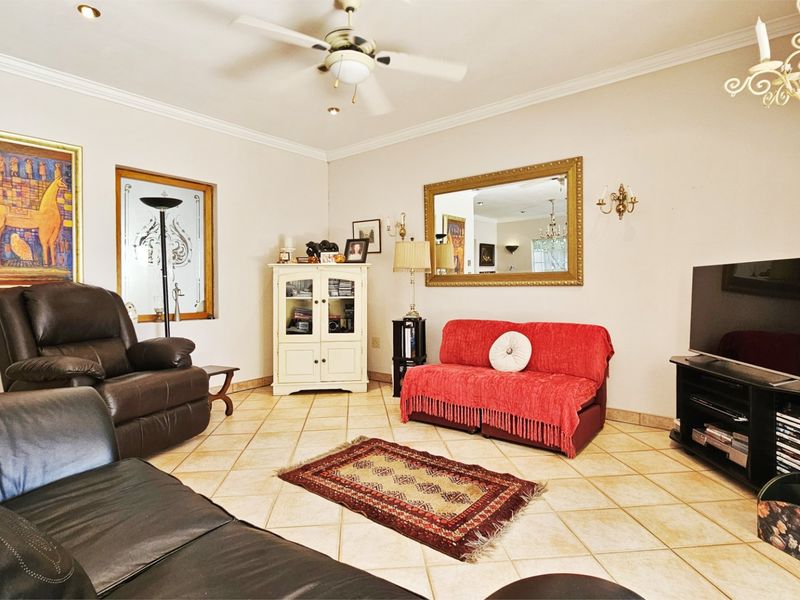 A spacious living room featuring tiled flooring, a ceiling fan, and decorative cornice detailing, offering a comfortable and functional layout.