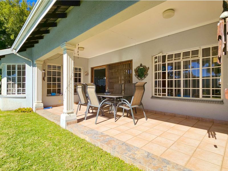 A covered patio area featuring tiled flooring, decorative columns, and access to the interior through sliding glass doors, overlooking a garden space.