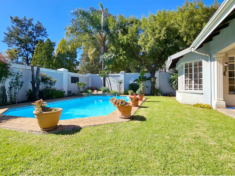A well-maintained backyard featuring a swimming pool with brick coping, a manicured lawn, and a covered patio area.