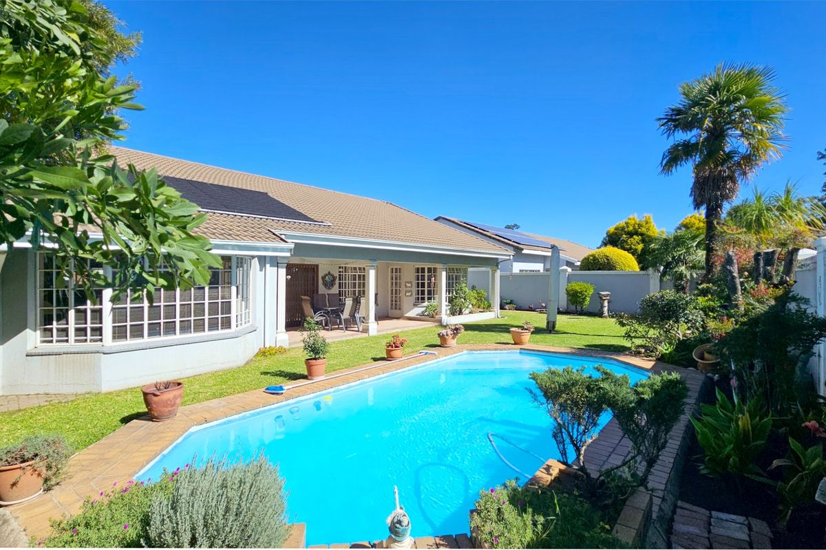 Rear exterior view of the townhouse featuring a swimming pool, paved surround, covered patio, and well-maintained garden with solar panels on the roof.