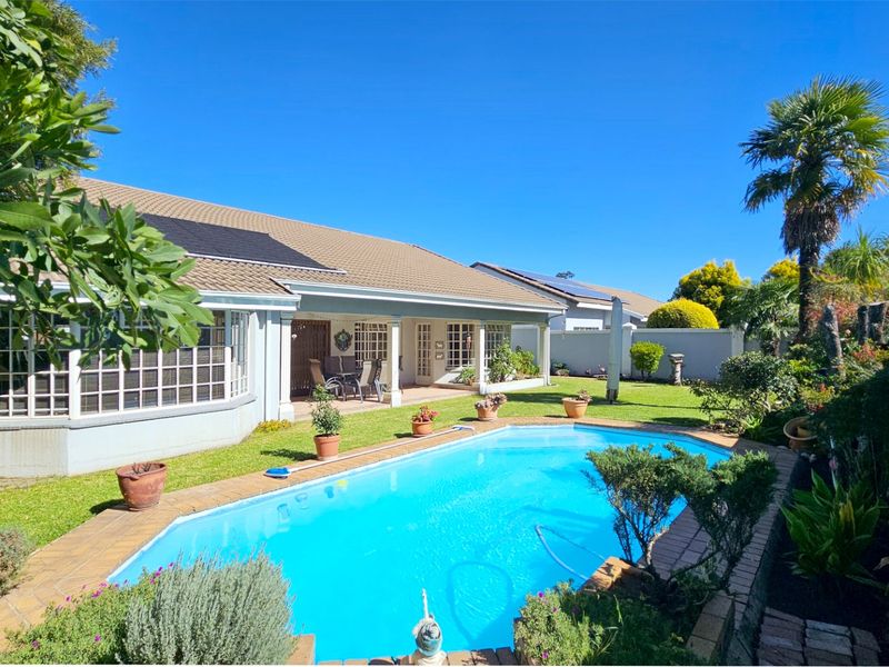 Rear exterior view of the townhouse featuring a swimming pool, paved surround, covered patio, and well-maintained garden with solar panels on the roof.