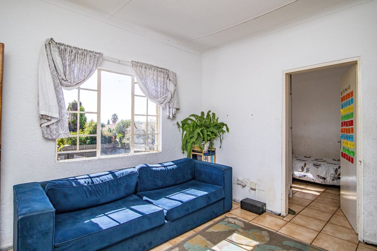A living room featuring tiled flooring and a steel-framed window, showing signs of wear and wall damage requiring maintenance.